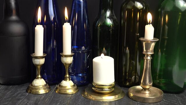The flame of a burning candle in a brass candlestick is extinguished by a breath of wind. Burning white candles in old vintage brass and bronze candlesticks against the background of glass multicolore