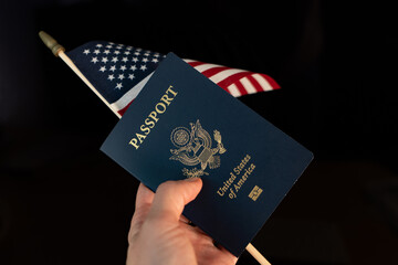 Hand holding a passport of USA and  flag of USA on a black blurred background