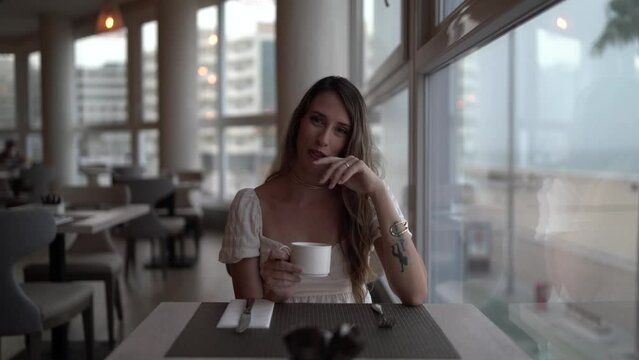 Chica joven en cafeter&iacute;a restaurante de hotel de lujo tomando bebida caliente mirando por la ventana y visitando el establecimiento