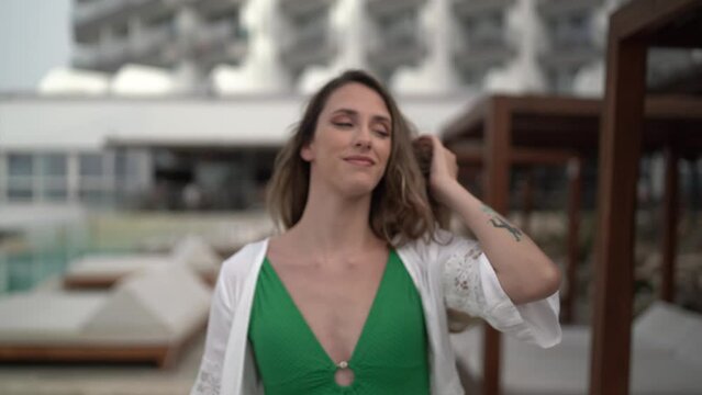 chica joven con pelo largo paseando por piscina de hotel en ropa de ba&ntilde;o