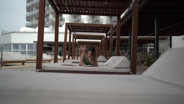 Chica joven en hamaca de piscina de hotel leyendo y disfrutando de las vacaciones