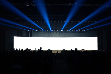 Front view of mockup on big blank white screen with space in huge hall and silhouette of audiences
