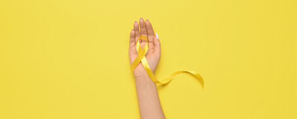 Hand with golden awareness ribbon on yellow background. Cancer concept