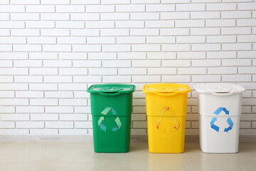 Different garbage bins with recycling symbol near white brick wall
