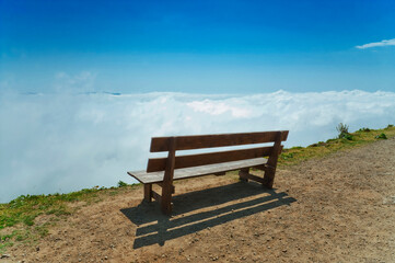 Bench without people on precipice above the clouds.