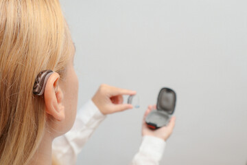 Blond woman Inserts Hearing Aid on ear at home. Deafness treatment, hearing solutions. Deaf woman...