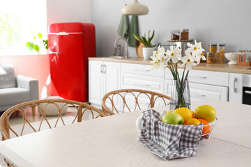 Basket with fruits and narcissus flowers on table in light kitchen, closeup