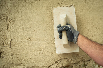 "A worker smoothes the material applied to a stone wall with a trowel."