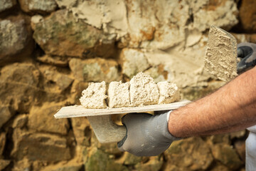 A laborer applies a product to a stone wall with a trowel to begin construction.