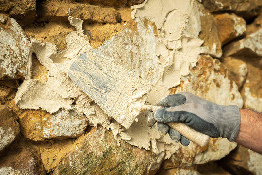 A laborer applies a product to a stone wall with a trowel to begin construction.