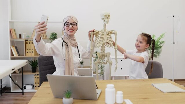 Doctor taking selfie with little kid near skeleton at work