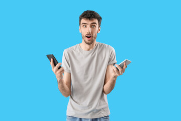 Surprised young man with mobile phones on blue background