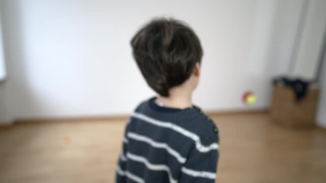 Child hitting ball with racket against bedroom wall at home, kid practices tennis inside empty bedroom apartment. Little boy exercising, future champion