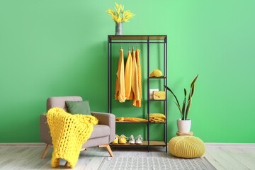 Interior of stylish room with shelving unit, clothes and armchair