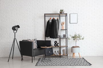 Interior of modern room with shelving unit, suits and armchair