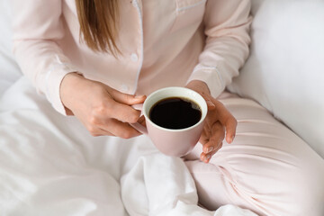 Woman holding cup of delicious coffee in bed