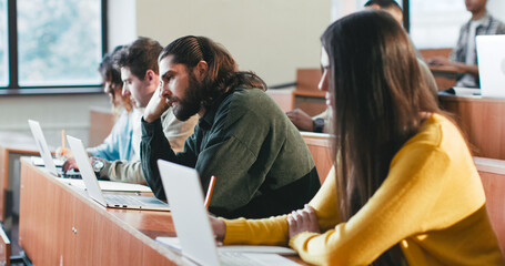 Bored students, males and females sittingat desk at college lesson and listening to professor....