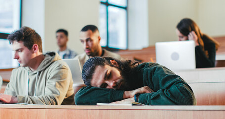 Caucasian male handsome student sleeping on desk at lection in college. Young man having a nap at...