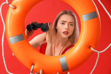 Worried female lifeguard with binoculars and ring buoy on red background