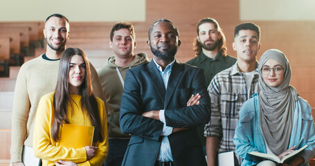 Portrait shot of African American male happy professor among mixed-races students in auditorium of University laughing n front of camera. Teacher and pupils concept. Posing for photo.
