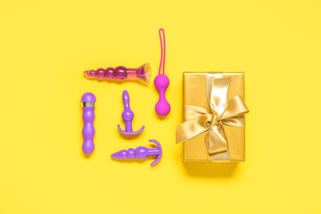 Composition with different sex toys and gift box on yellow background