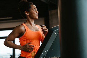 Proud happy young woman running on a treadmill in the fitness gym and looking aside.