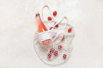 Mesh bag with fresh strawberry and bottle of juice on white background