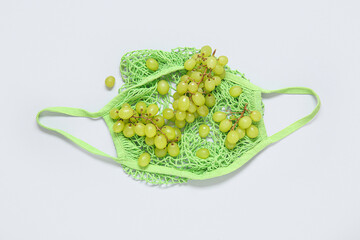 Mesh bag with fresh grapes on white background