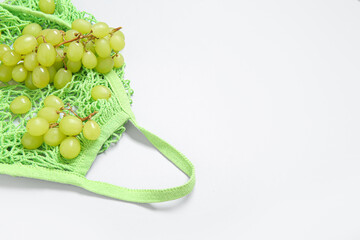 Mesh bag with fresh grapes on white background, closeup