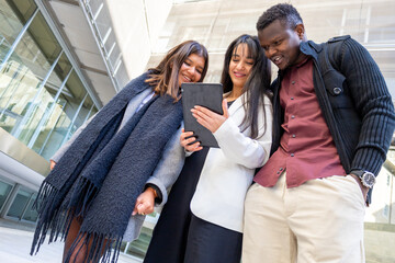 Smiling coworkers using a tablet at office outdoors. Group of young friends meeting in the city. Ethnic diversity.