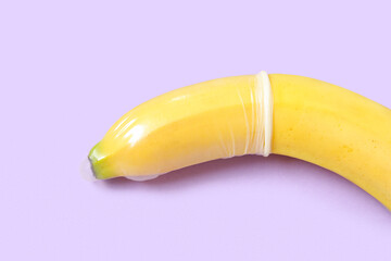 Fresh banana in condom on purple background, closeup. Sex education concept