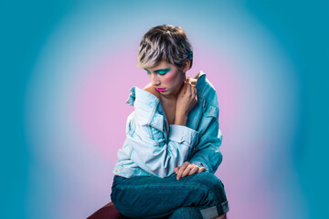 young pretty woman with make up and fashion sit on pink and blue background with hand to head and...