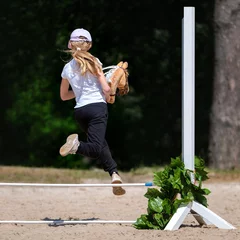 Poster Girl jumping on hobby horse. Champion. Horse sport. Summer light. Green outdoor trees background. The Cavaletti route. Child sport. Banner © mari