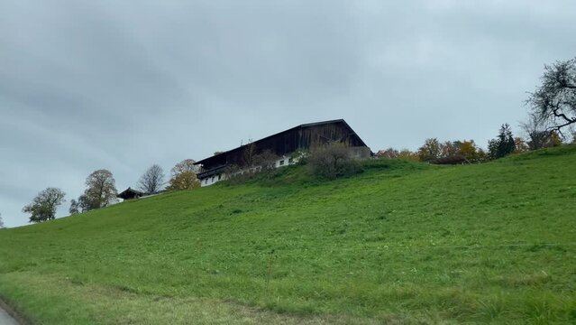 Views of countryside house on top of hill from inside car driving on Thiersee town road in Austria on cloudy day