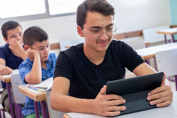 Teenager using the tablet in school and have a smile on his face - obrazy, fototapety, plakaty