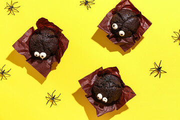 Delicious chocolate cupcakes and spiders for Halloween celebration on yellow background