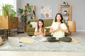 Asian mother with her little daughter meditating at home - obrazy, fototapety, plakaty