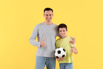 Little boy with his dad holding soccer ball on yellow background
