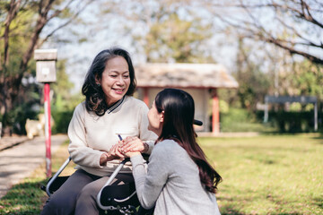 Senior on wheelchair and daughter family concept, Young asian woman holding hands to encourage mother on wheelchair while senior woman and daughter relaxation with talking in the park