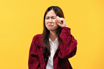 Young asian woman wearing red jacket and wipe the tears by hand while feeling sad and crying...