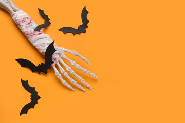 Skeleton hand and paper bats for Halloween celebration on orange background