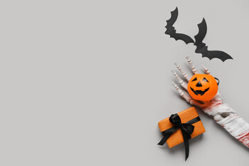 Skeleton hand with pumpkin, gift box and paper bats for Halloween celebration on grey background
