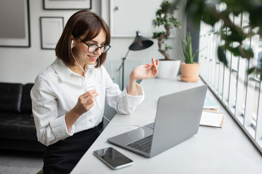 Distance Communication Concept. Woman Manager In Earphones Teleconferencing Via Laptop, Sitting At Workplace In Office