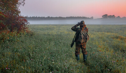  Hunter looks through binoculars in autumn in the fog at the edge of the forest.