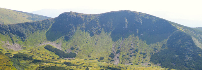 mountain range with vegetation and a cliff face and a blue sky.