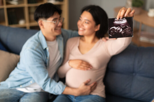Happy pregnant asian couple showing ultrasound image at home