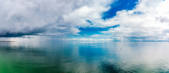 Fototapeta na wymiar Storm Clouds Gathering Over Ocean. dark clouds are gathering. bad weather coming. Bright beautiful seascape, clouds reflected in the water, natural minimalistic background and texture, panoramic view 