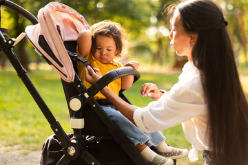 Mom Caring For Daughter's Comfort During Walk In Stroller Outside