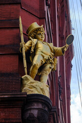 golden statue of a boy  against a old brick building