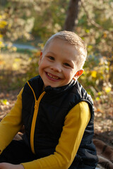 Portrait of a boy in the autumn forest. the boy looks at the camera and smiles happily. Boy dressed in a yellow sweater and a black vest 